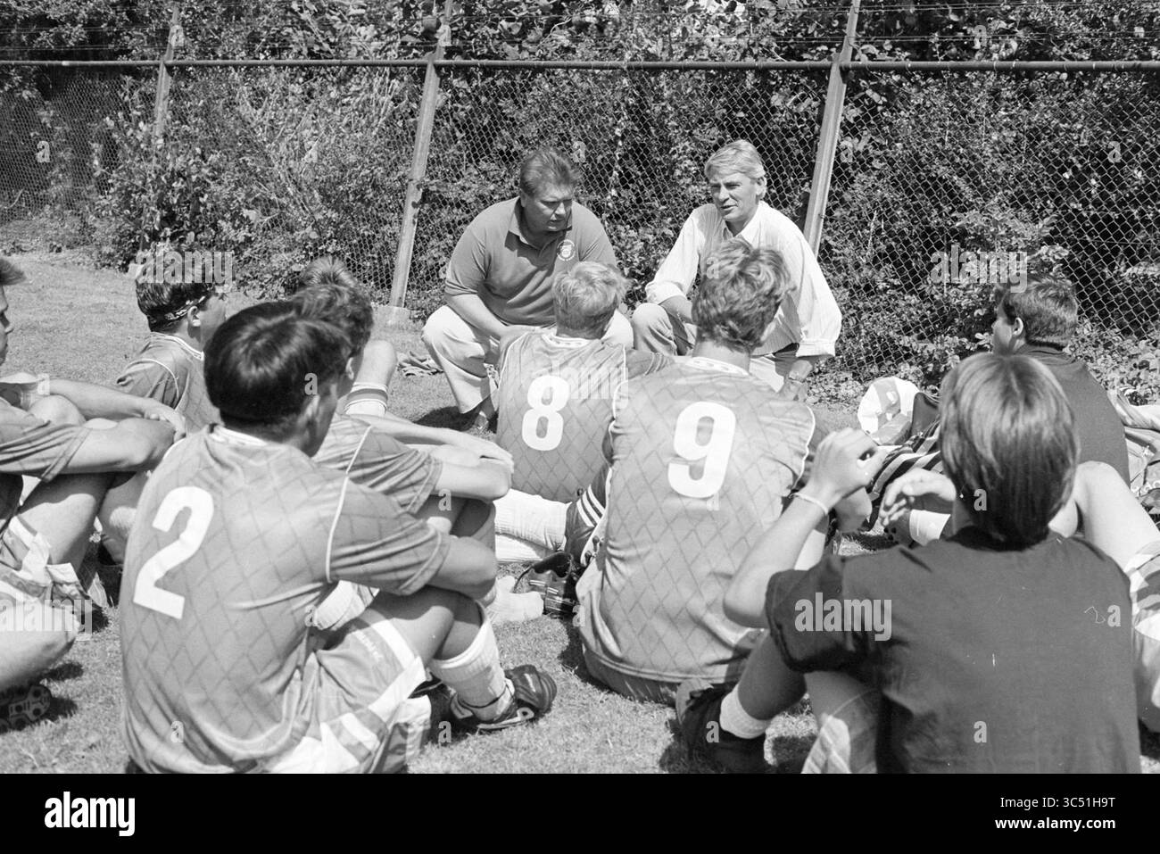 Football tournament Haarlem Cup, Ted Immers speaks with a football team, Haarlem, The Netherlands, 04-08-1992 Whizgle News, Dutch Desk, The Netherlands, 1950-2000 A group of young soccer players attentively listens to their coaches during a training session, gathering on the field in a circle. The coaches engage in a discussion, emphasizing teamwork and strategy as the players, wearing numbered jerseys, sit cross-legged on the grass. Stock Photo