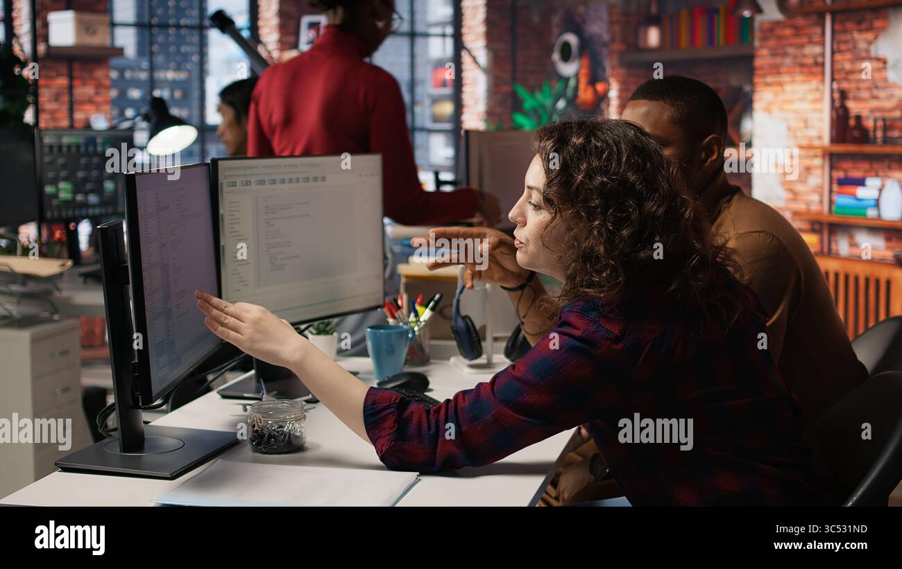 Startup programmer collaborating with colleague to test company software, identifying bottlenecks. Team of engineers writing clean, efficient code in programming language to reduce errors, camera A Stock Photo