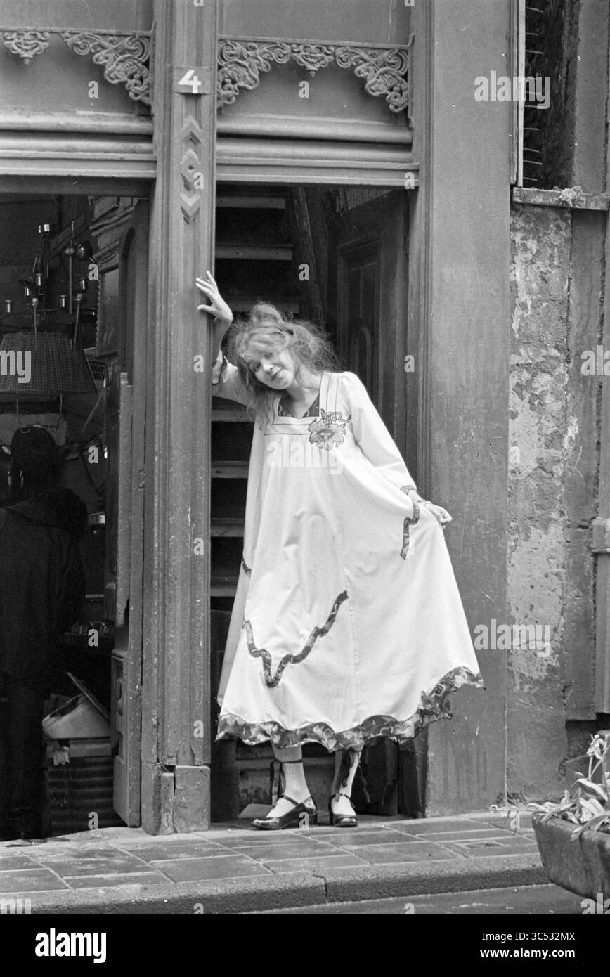 Aenne van. Brederode fashion designer, Fashion photos, 13-05-1975 Whizgle News, Dutch Desk, The Netherlands, 1950-2000 A young woman stands gracefully in a doorway, wearing a flowing dress adorned with decorative trim. Her playful pose and vibrant expression contrast with the rustic backdrop, suggesting a sense of spontaneity and charm in a bustling environment. Stock Photo