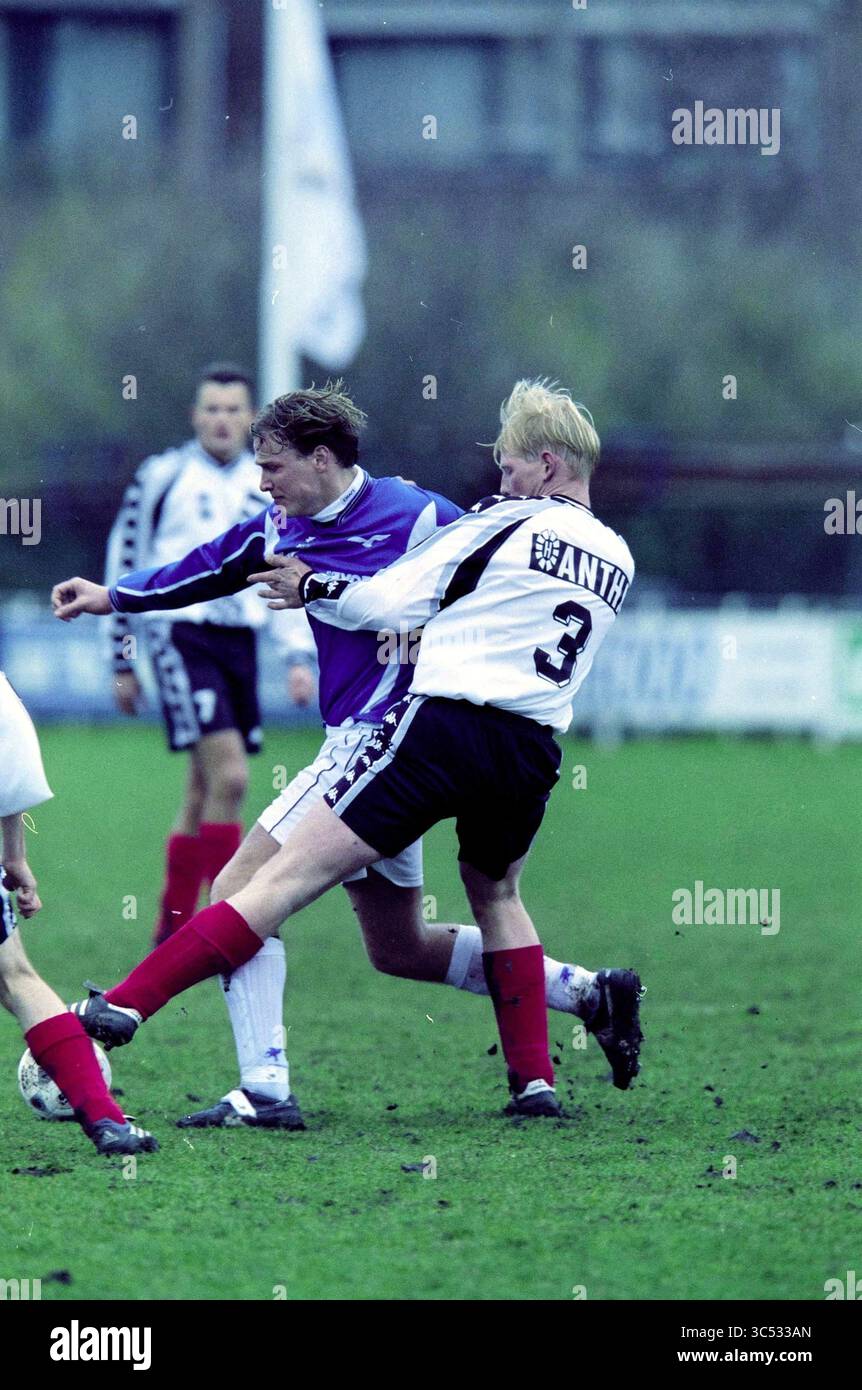 Football: VSV - Beverwijk, 17-03-2001 Whizgle News, Dutch Desk, The Netherlands, 1950-2000 A competitive moment in a soccer match, where one player aggressively challenges another, showcasing the intensity of the game. The players are in dynamic motion, with one in a purple jersey and the other in a white and black ensemble, set against a grassy field. Stock Photo