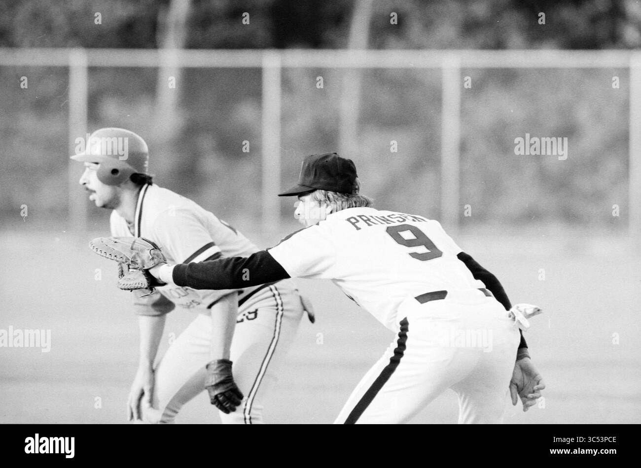 Han Prinsen, Baseball Haarlem Nicols, 28-05-1986 Whizgle News, Dutch Desk, The Netherlands, 1950-2000 A baseball player in a white uniform with the number 9 crouches in a ready position at first base, while a player in an orange helmet and grey uniform stands at the edge of a leading position on second base, both poised for the next play. The background suggests a baseball field setting. Stock Photo