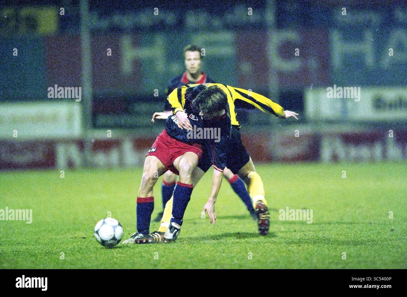 Football: Haarlem - BV Veendam, Haarlem, The Netherlands, 20-03-2003 Whizgle News, Dutch Desk, The Netherlands, 1950-2000 Two soccer players are engaged in a fierce battle for possession of the ball. One player, wearing a red and black kit, bends forward to regain control, while the other, in a yellow and black striped shirt, attempts to tackle from behind. The competitive tension is palpable as they vie for dominance on the field. Stock Photo