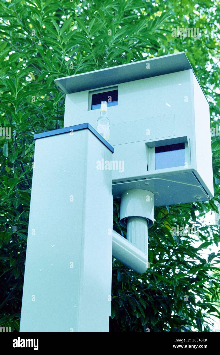 Flash box bottle, Overveen, Overveen, 23-08-2000 Whizgle News, Dutch Desk, The Netherlands, 1950-2000 A sleek, modern surveillance camera is mounted on a pole, partially obscured by lush green foliage, observing its surroundings with a watchful gaze. Stock Photo