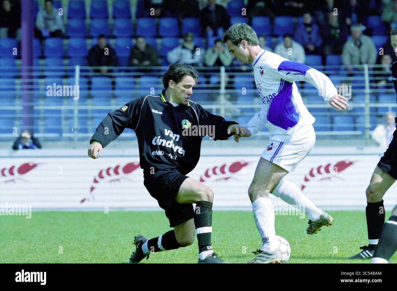 Football Telstar - Fc The Hague, 06-04-2002 Whizgle News, Dutch Desk, The Netherlands, 1950-2000 A dynamic moment on the soccer field captures two players in an intense challenge for the ball, showcasing athleticism and determination amidst a backdrop of spectators. One player, dressed in a black kit, tries to evade the tackle from the opposing player in white and purple. Stock Photo