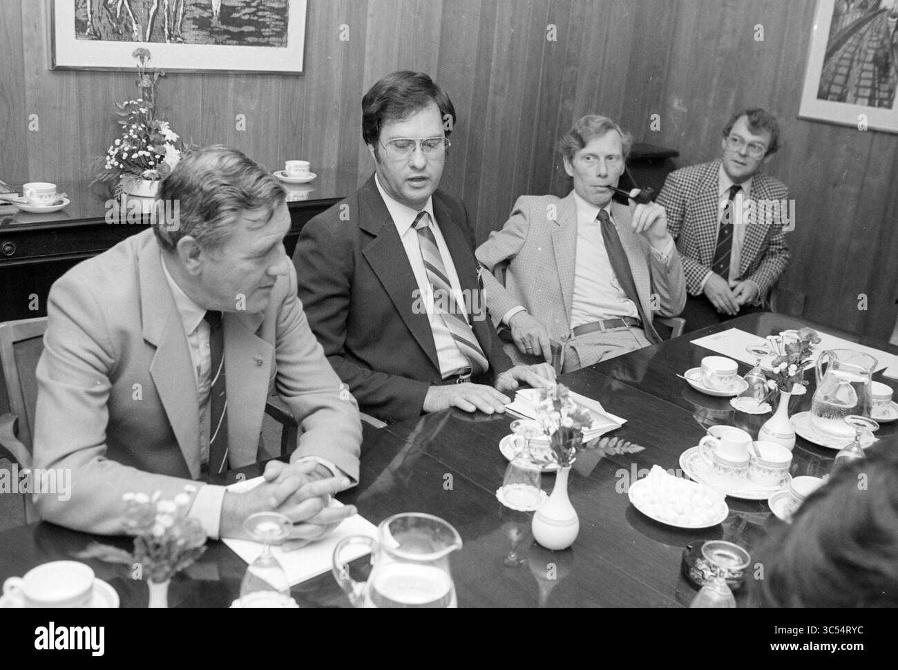 Press meeting IAAP Amsterdam airport police, Meetings, Aviation, aerial photos, Amsterdam, The Netherlands, 25-05-1984 Whizgle News, Dutch Desk, The Netherlands, 1950-2000 A group of men engages in discussion around a table set with tea and snacks, surrounded by a warm wooden environment. Each individual showcases distinct attire and expressions, contributing to the atmosphere of a formal gathering. Stock Photo