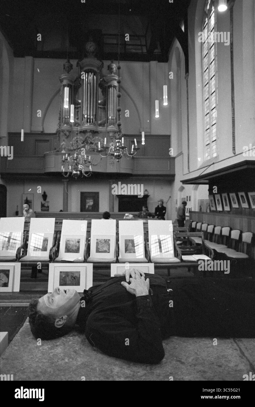 Singing opera in the Walloon Church, Begijnhof, Haarlem, Begijnhof, The Netherlands, 05-11-1993 Whizgle News, Dutch Desk, The Netherlands, 1950-2000 A man lies on the floor of a spacious church, gazing upwards at an elaborate organ and high ceilings, while framed artworks are displayed on tables nearby. Stock Photo