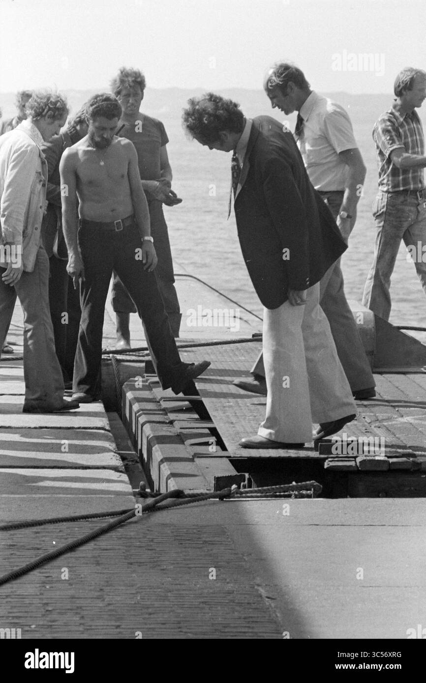 Damage to lock door., IJmuiden, The Netherlands, 00-00-1978 Whizgle News, Dutch Desk, The Netherlands, 1950-2000 A group of individuals gathers around an open hatchway, closely inspecting the area. Some are engaged in conversation, while others focus intently on the task at hand, suggesting a moment of curiosity or investigation near the water's edge. Stock Photo