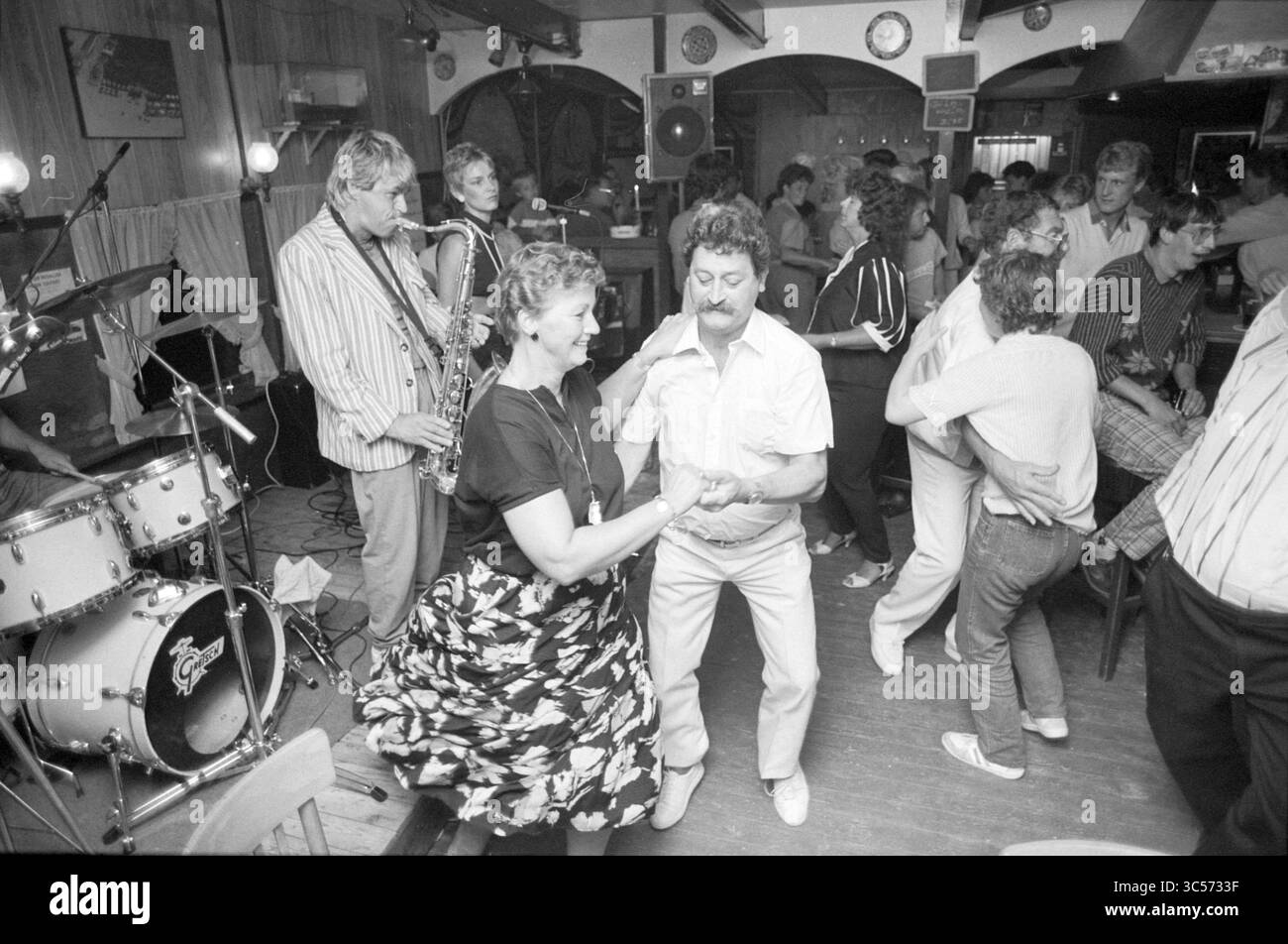 Dancing in the North Sea pavilion, IJmuiden, Dancing, IJmuiden, The Netherlands, 26-07-1986 Whizgle News, Dutch Desk, The Netherlands, 1950-2000 A lively dance floor scene where couples enjoy a spirited evening, swaying to live music from a saxophonist and a drum set. The atmosphere is filled with laughter and movement as people of varying ages engage in joyful dancing, showcasing a sense of camaraderie and celebration. Stock Photo