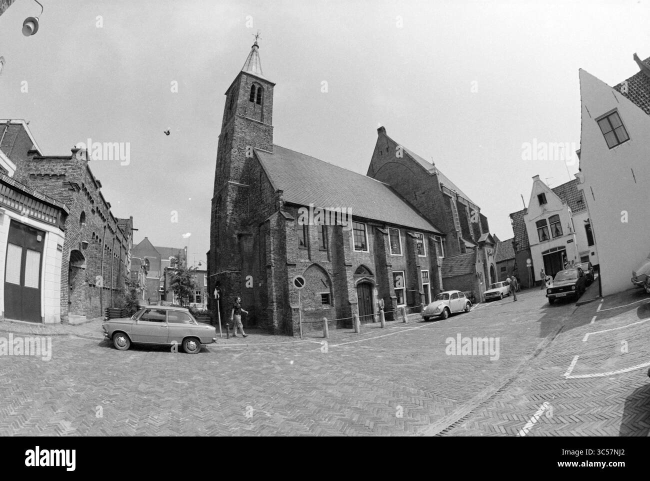 Exterior Walloon Church (photo with distorting lens), Haarlem, Begijnhof, The Netherlands, 31-05-1979 Whizgle News, Dutch Desk, The Netherlands, 1950-2000 A quaint street corner showcases charming old buildings, including a historic church with a tall steeple. Classic cars are parked nearby, while pedestrians stroll along the cobblestone path, adding to the serene, nostalgic atmosphere. Stock Photo