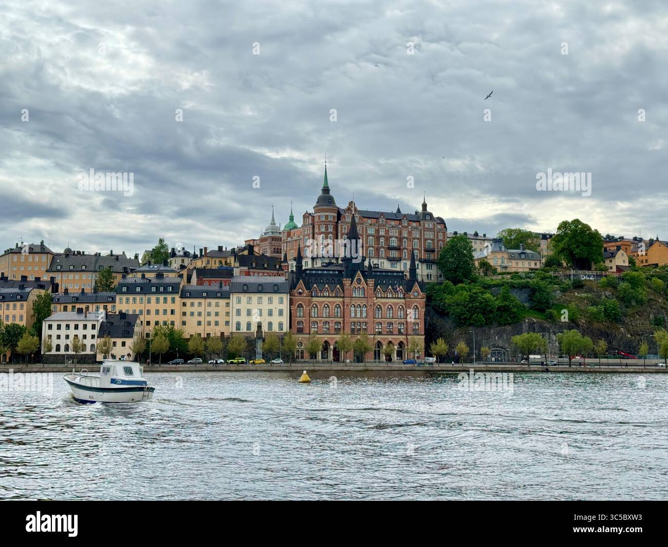 View of Södermalm in Stockholm, Sweden, seen from across the water. A small boat in the foreground contrasts with historic buildings and rich greenery - Smartphone Captured Stock Image