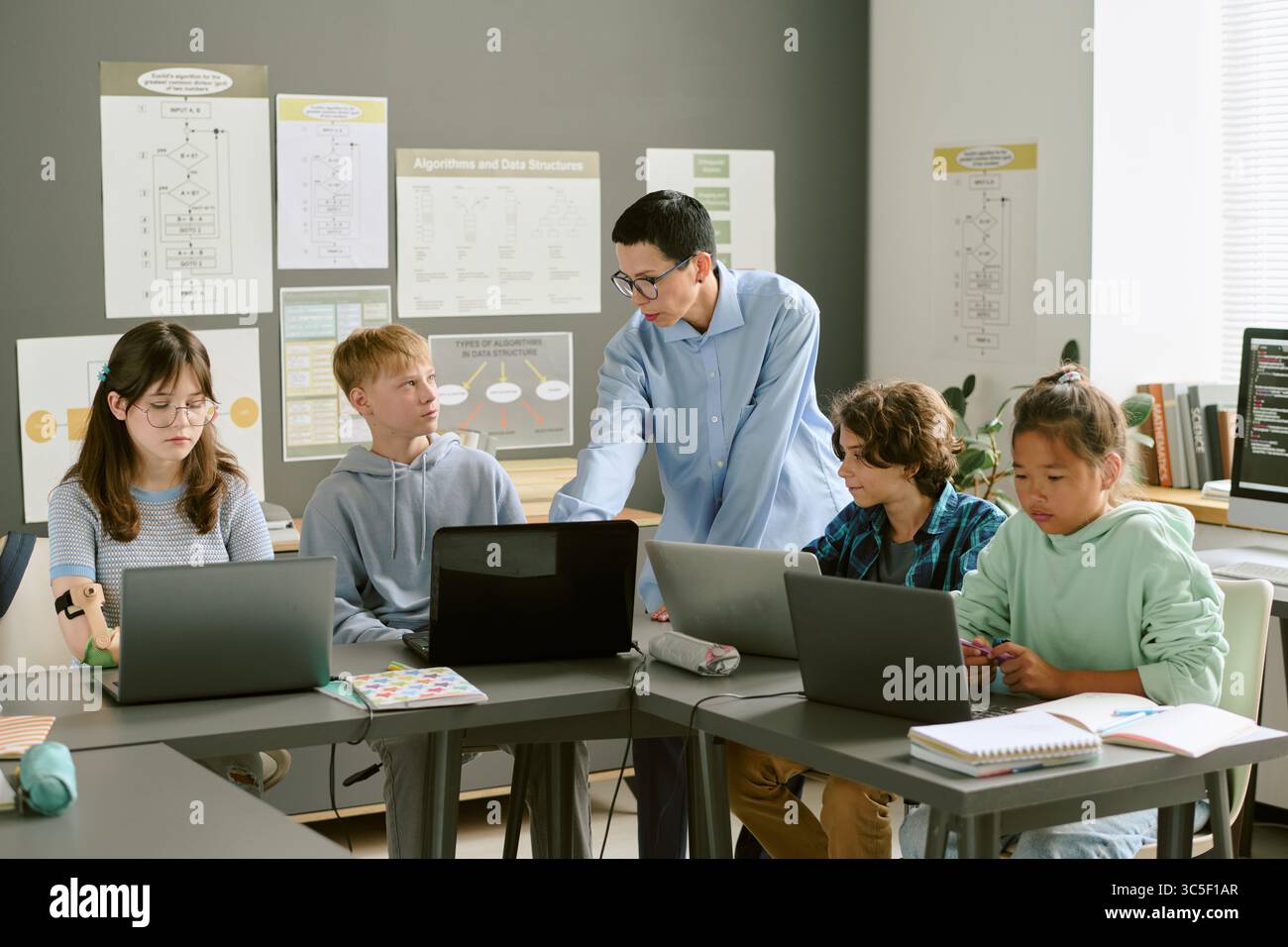 Teacher Instructing Diverse Teenagers Using Laptops in Classroom Stock Photo