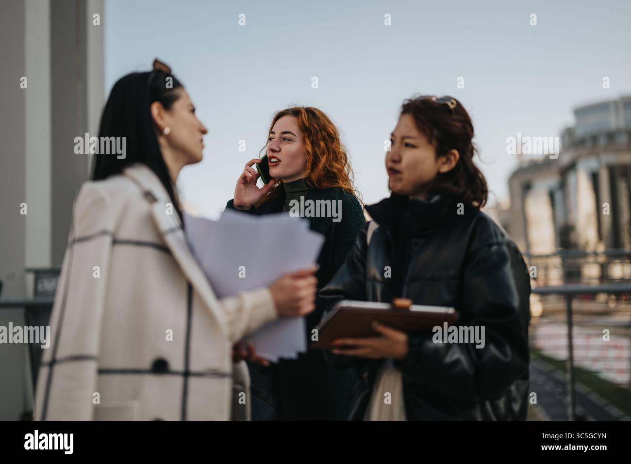 Three Women Collaborating Outdoors with Documents and Communication Tools Stock Photo