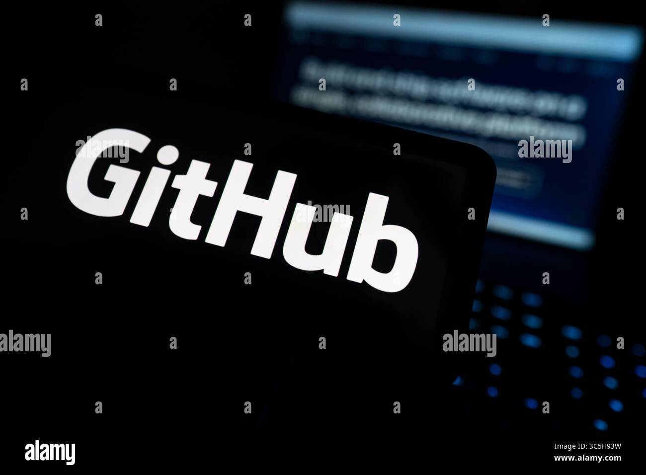 GitHub Logo Displayed On Computer Screen With Code Repository Open In Background Stock Photo