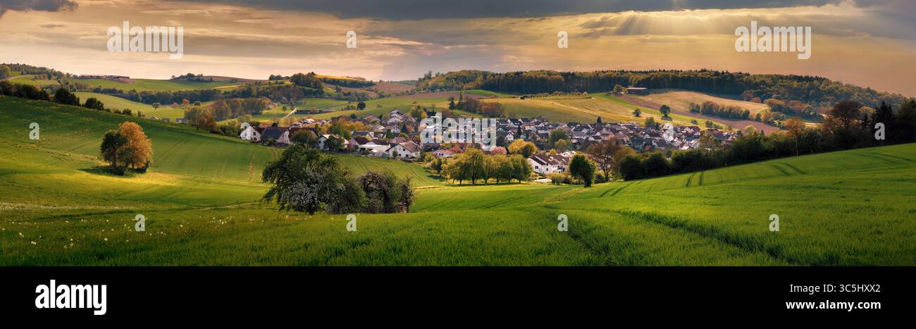 Village in a valley in golden dramatic light. A panoramic tranquil rural scenery with a scenic small town surrounded with green meadows on hills Stock Photo