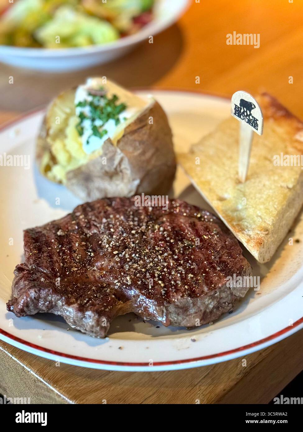 A deliciously prepared steak served with a baked potato, topped with fresh chives, and accompanied by a slice of garlic bread at Block House restauran - Smartphone Captured Stock Image