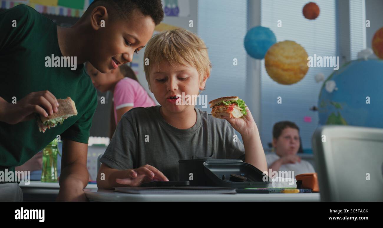 Primary School Boy Sitting at Desk, Eating Sandwich from Lunch Box ...