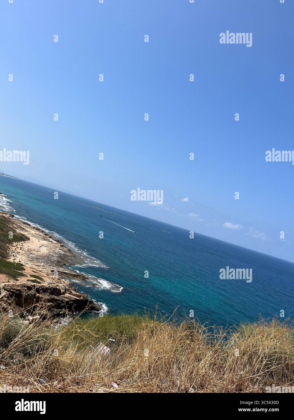 Rosh HaNikra coastline in Israel with turquoise Mediterranean water, dry coastal grasses, and scenic cliffs under a sunny blue sky on a bright summer - Smartphone Captured Stock Image