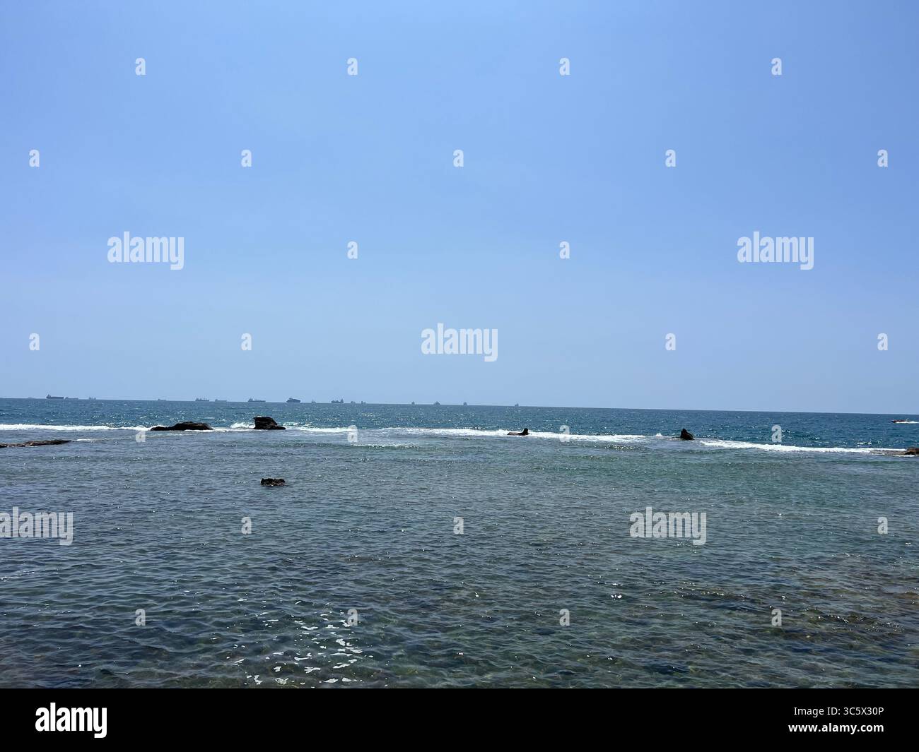 Shallow Mediterranean waters at Rosh HaNikra, Israel. Calm waves, clear sea floor, and distant swimmers under a bright blue sky near the Israeli coast - Smartphone Captured Stock Image