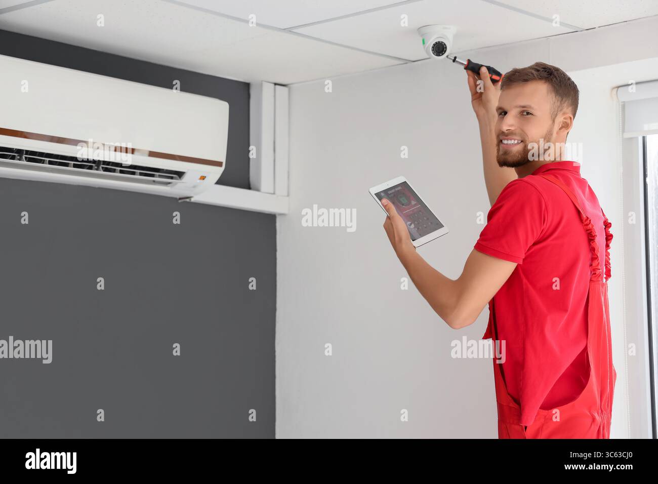 Male worker with tablet computer installing alarm system in room Stock Photo