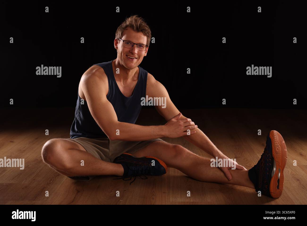young man doing floor training, stretching, black background Stock Photo