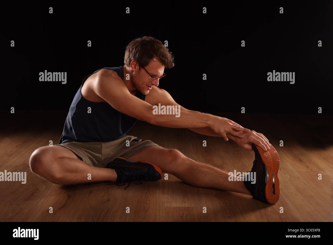 young man doing floor training, stretching with hand, black background Stock Photo