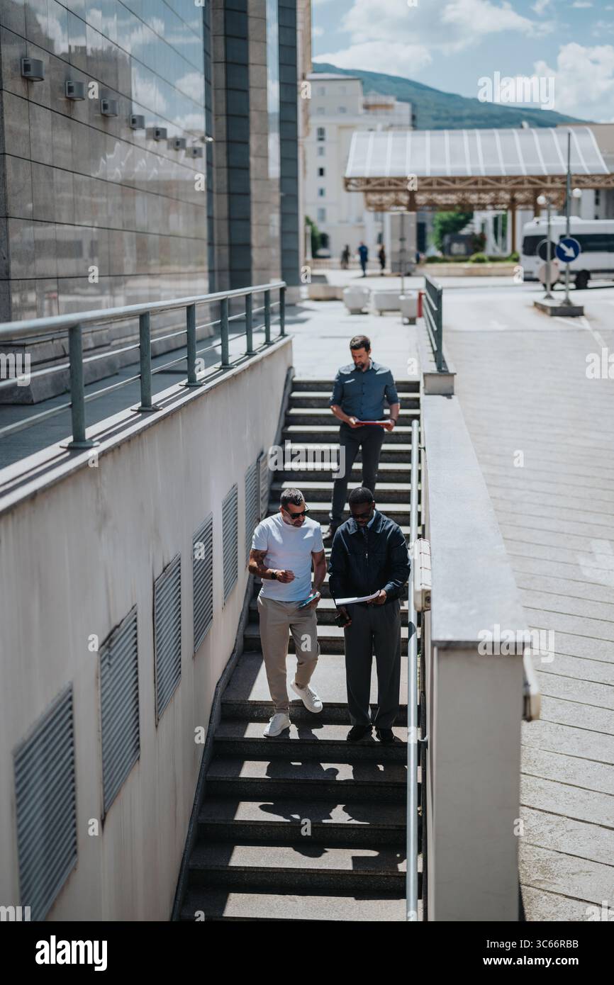 Three professionals discussing work documents while walking down outdoor stairs Stock Photo