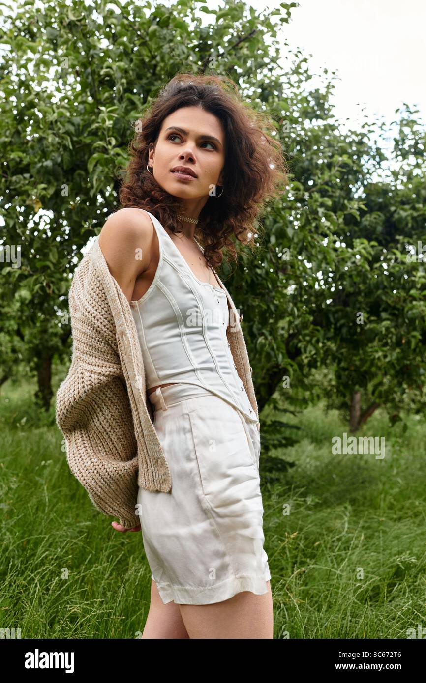 Curly-haired beauty showcases stylish summer fashion in a lush green park setting. Stock Photo
