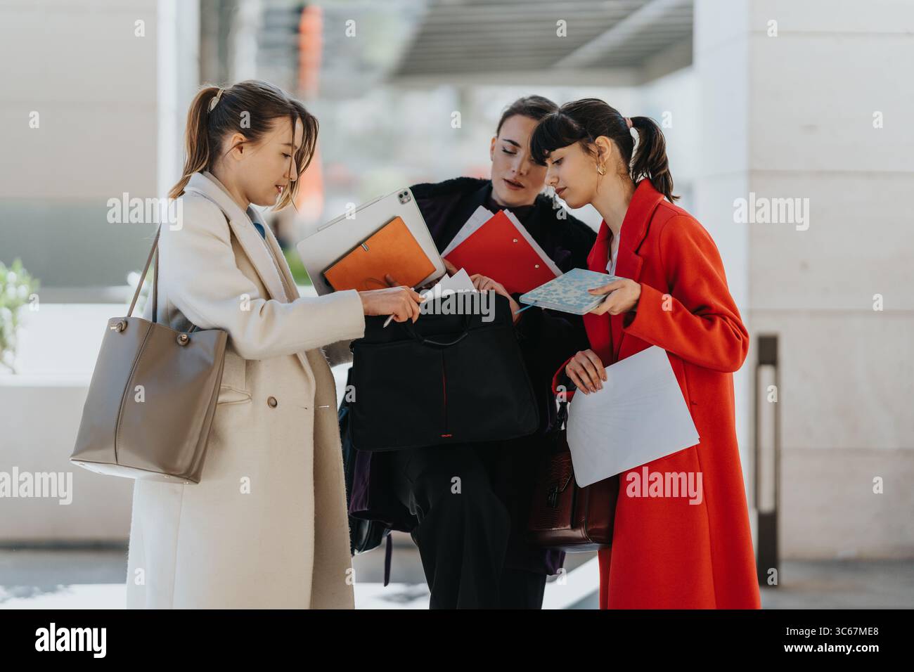Three female professionals collaborating on a project outdoors while reviewing documents Stock Photo