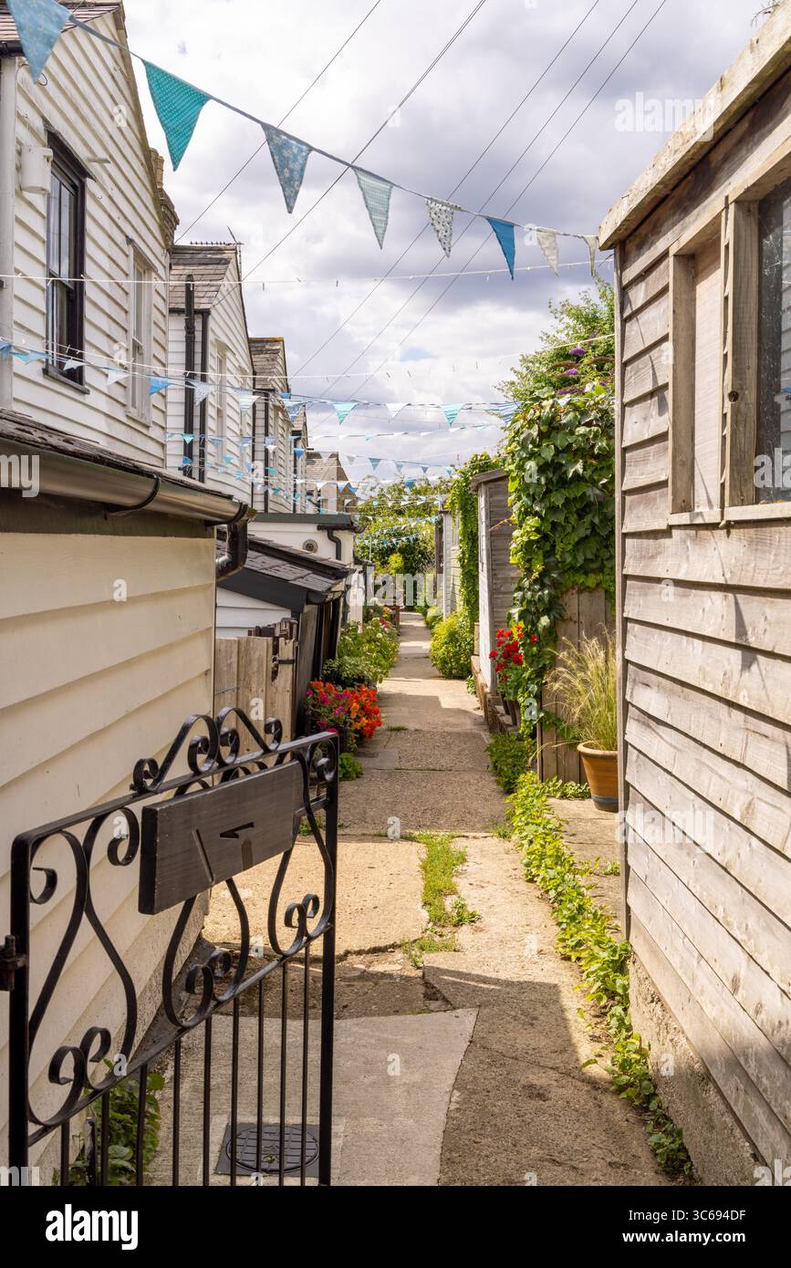 Narrow alleyway on  Terraces Leigh-on-Sea,, with colourful bunting, vibrant flowers, and traditional wooden houses on a summer day.  ?️ Keywords Stock Photo