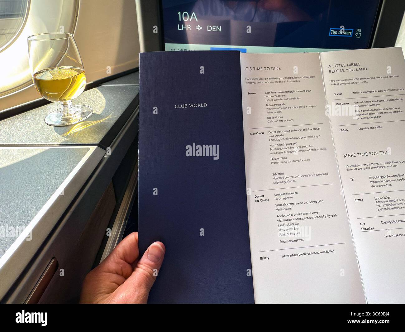 London, England, UK - 20 May 2025: Person reading the dinner menu in a Club World business class cabin seat with a glass of chilled champagne - Smartphone Captured Stock Image