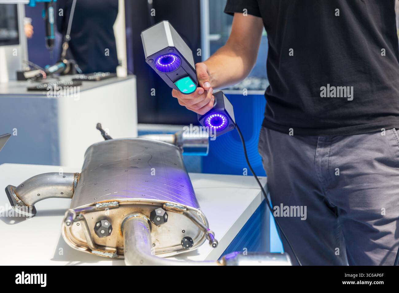 Close-up view of a technician using a handheld 3D laser scanner to scan an automotive exhaust component. The scanning process involves blue structured Stock Photo