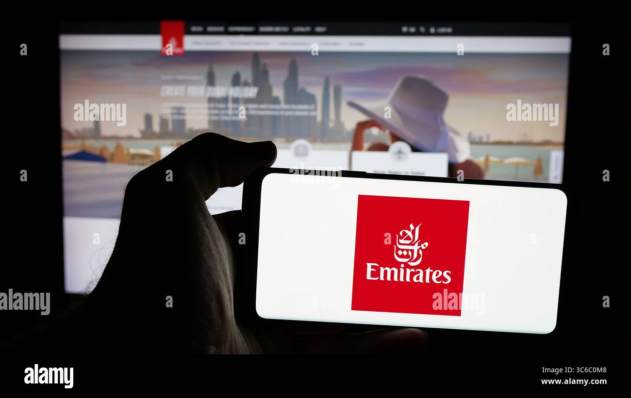 Stuttgart, Germany - 06-18-2025: Person holding mobile phone with logo of UAE airline company Emirates on screen in front of web page. Stock Photo