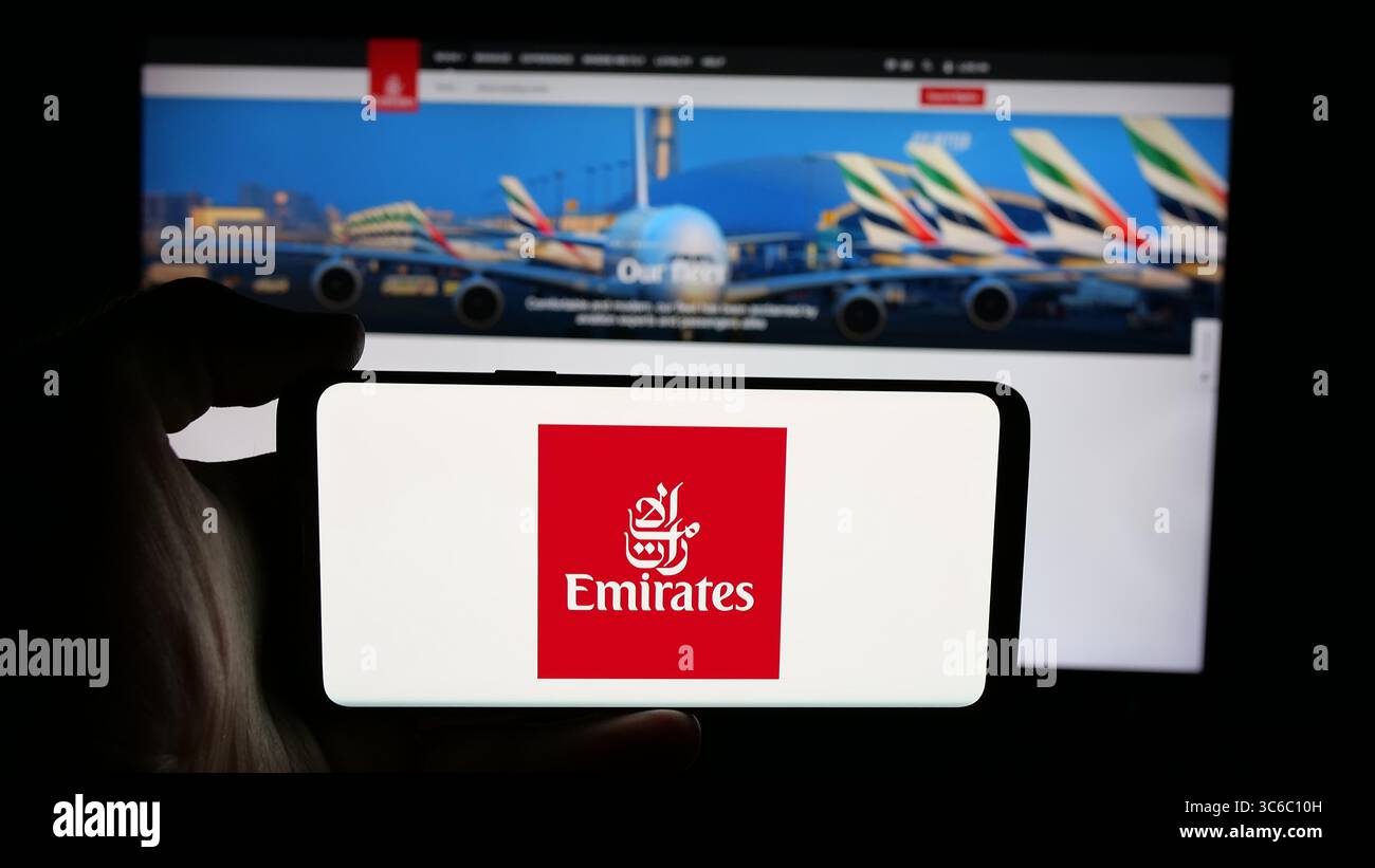 Stuttgart, Germany - 06-18-2025: Person holding cellphone with logo of UAE airline company Emirates on screen in front of webpage. Stock Photo