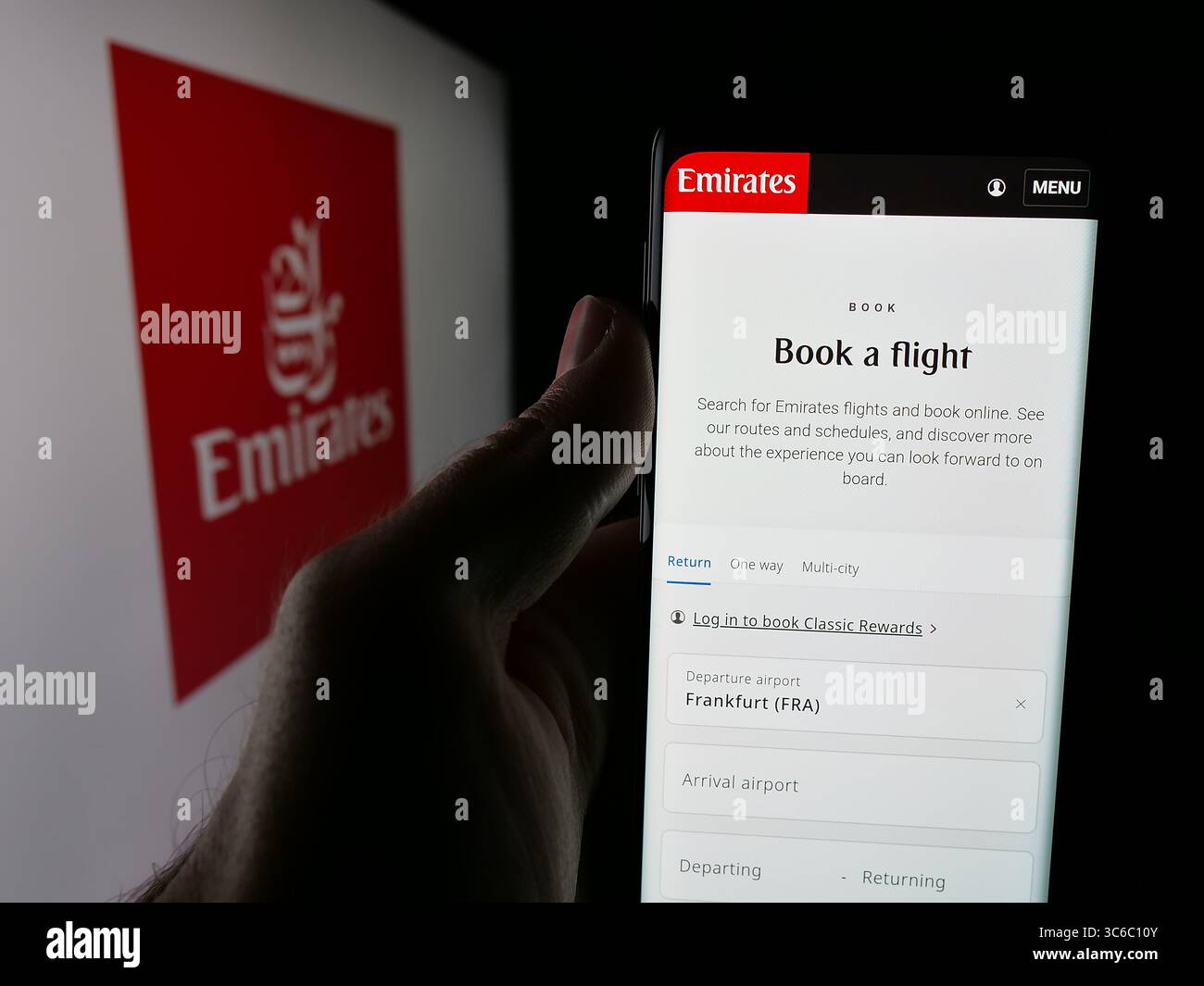 Stuttgart, Germany - 06-18-2025: Person holding cellphone with webpage of UAE airline company Emirates on screen in front of logo. Stock Photo
