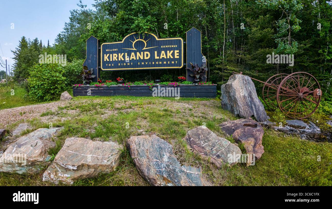 Kirkland Lake Welcome Sign is situated on Government Road West. Surrounding the sign are rocks, likely gold ore, with a rusty cart to the right of the Stock Photo