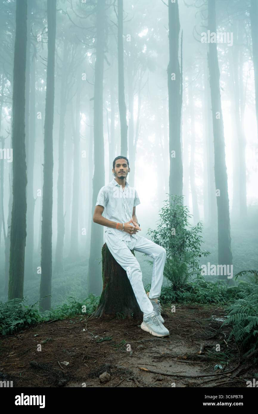 Self-portrait of a man sitting on a tree stump in a misty forest in Darjeeling, India. Captured during monsoon season with soft light filtering. Stock Photo
