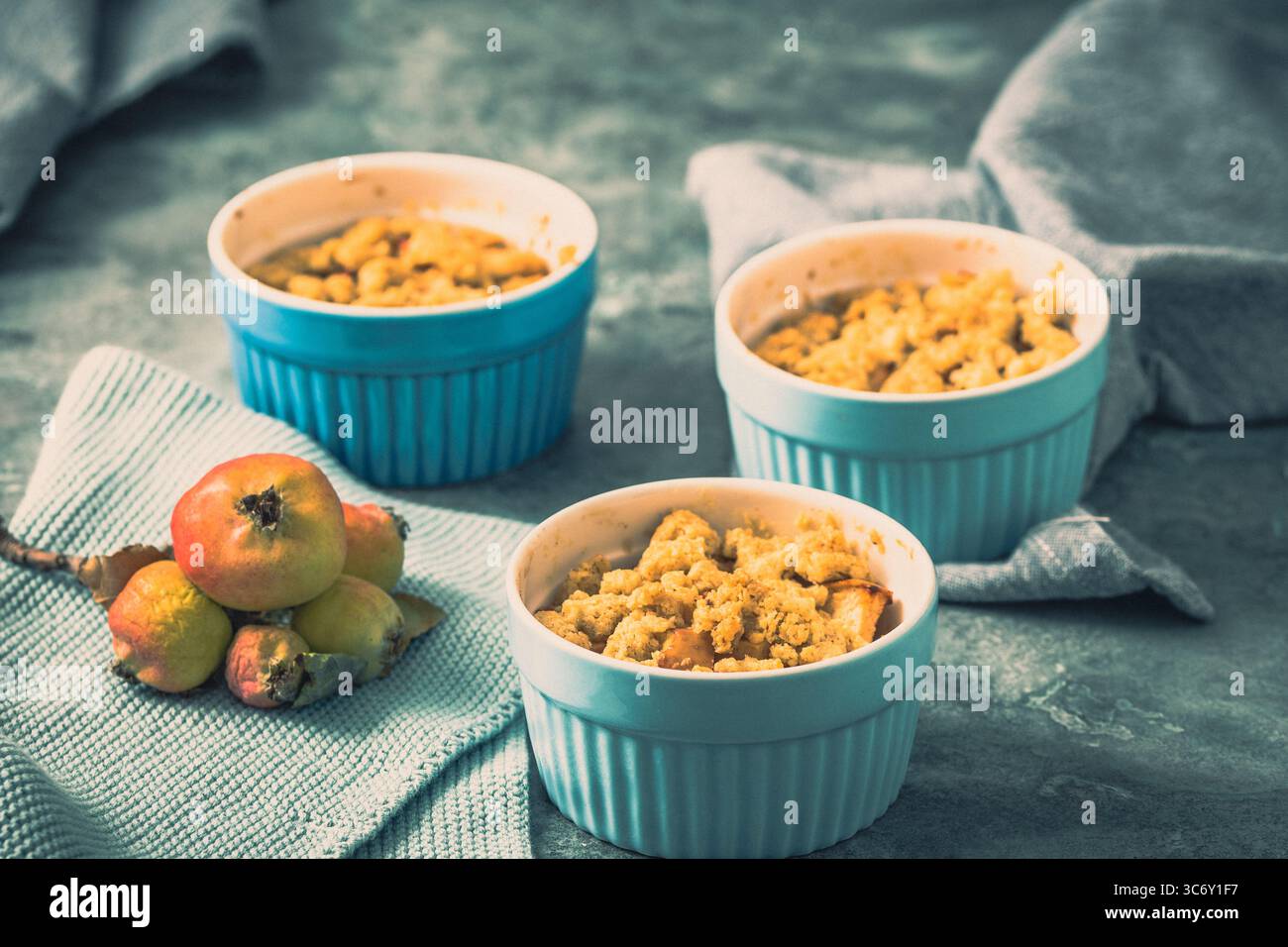 Apple crumble in small blue molds on a rustic gray table Stock Photo