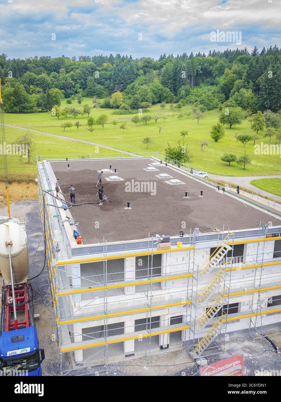 Partly completed building with workers in a landscaped environment ...