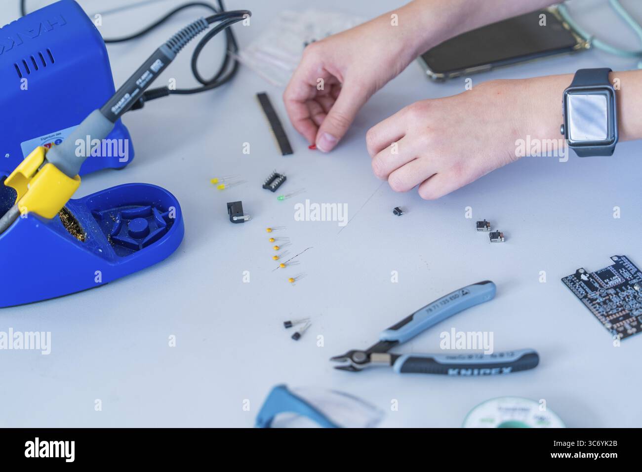 Working with electronic components on a table, soldering iron and hands clearly visible Stock Photo