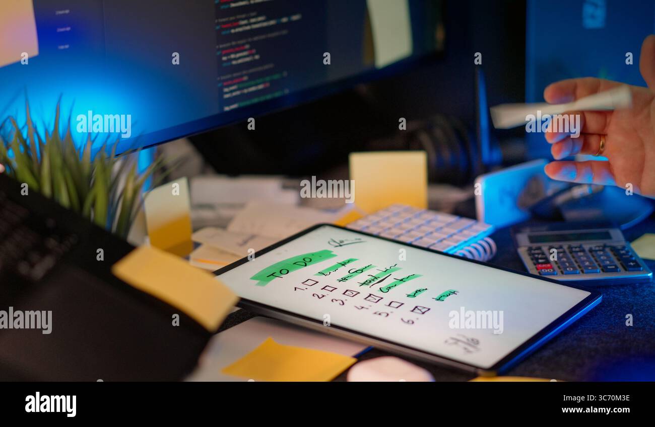 Checklist digital tablet task management workspace. Modern tech desk with digital tablet displaying handwritten to-do list, surrounded by coding monit Stock Photo