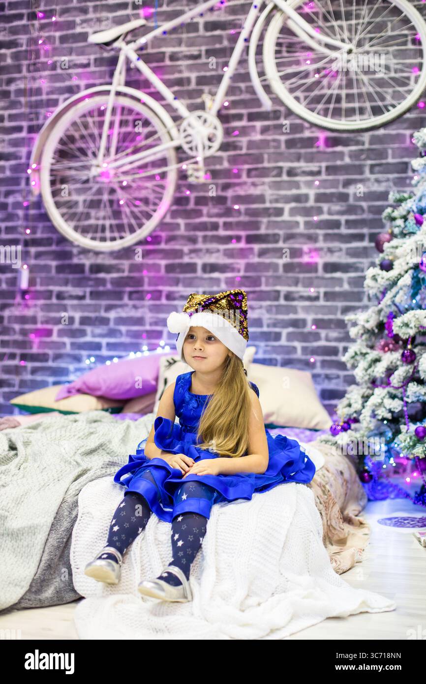 Pretty little girl 4 years old in a blue dress. Baby in Christmas room ...