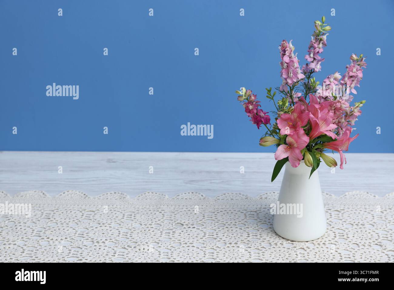 Beautiful flowers in vase on white wooden table against light blue ...