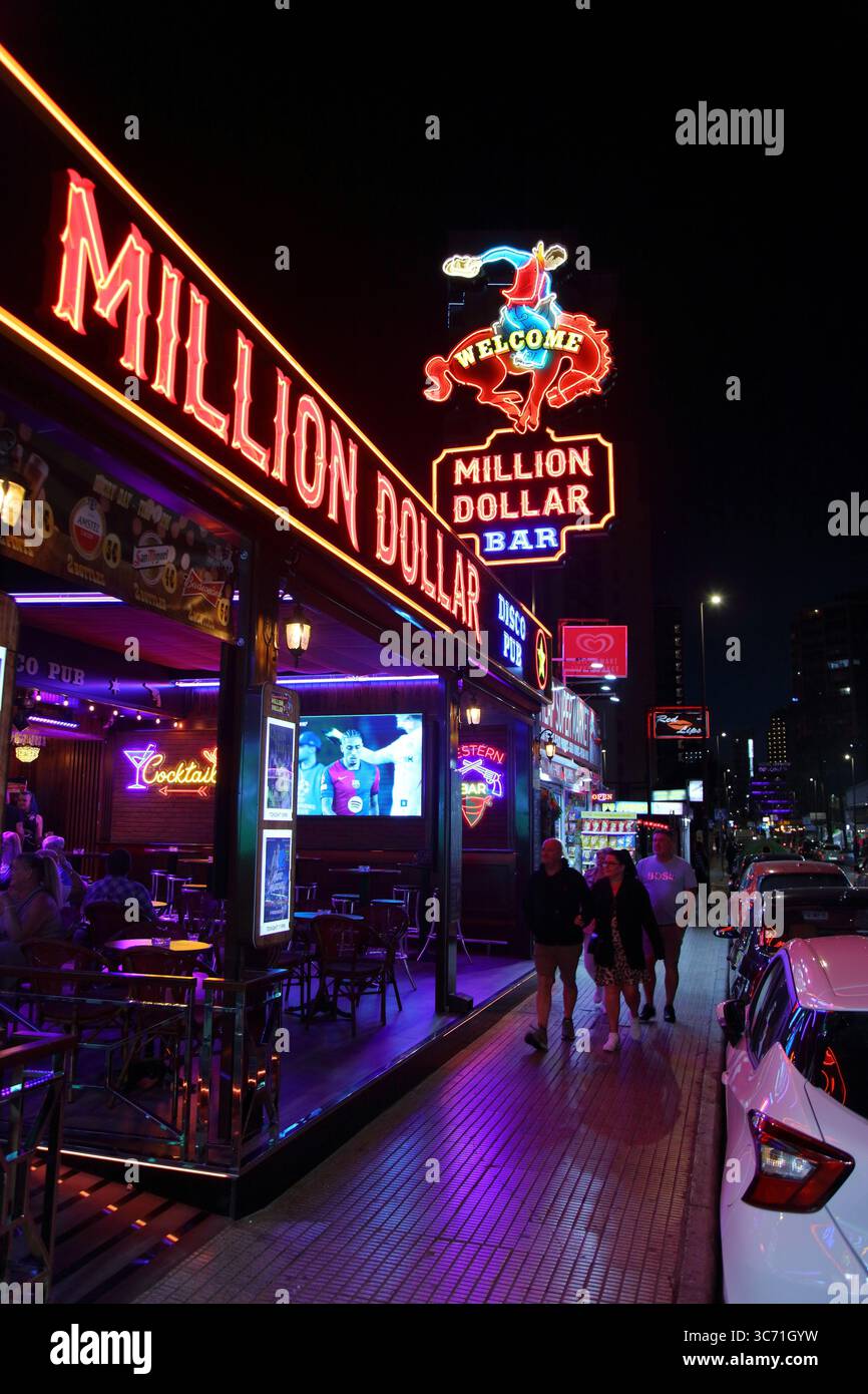 BENIDORM, SPAIN - APRIL 9, 2025: People visit Calle de Gerona street famous for its night life, with pubs, bars and restaurants illuminated with neons Stock Photo