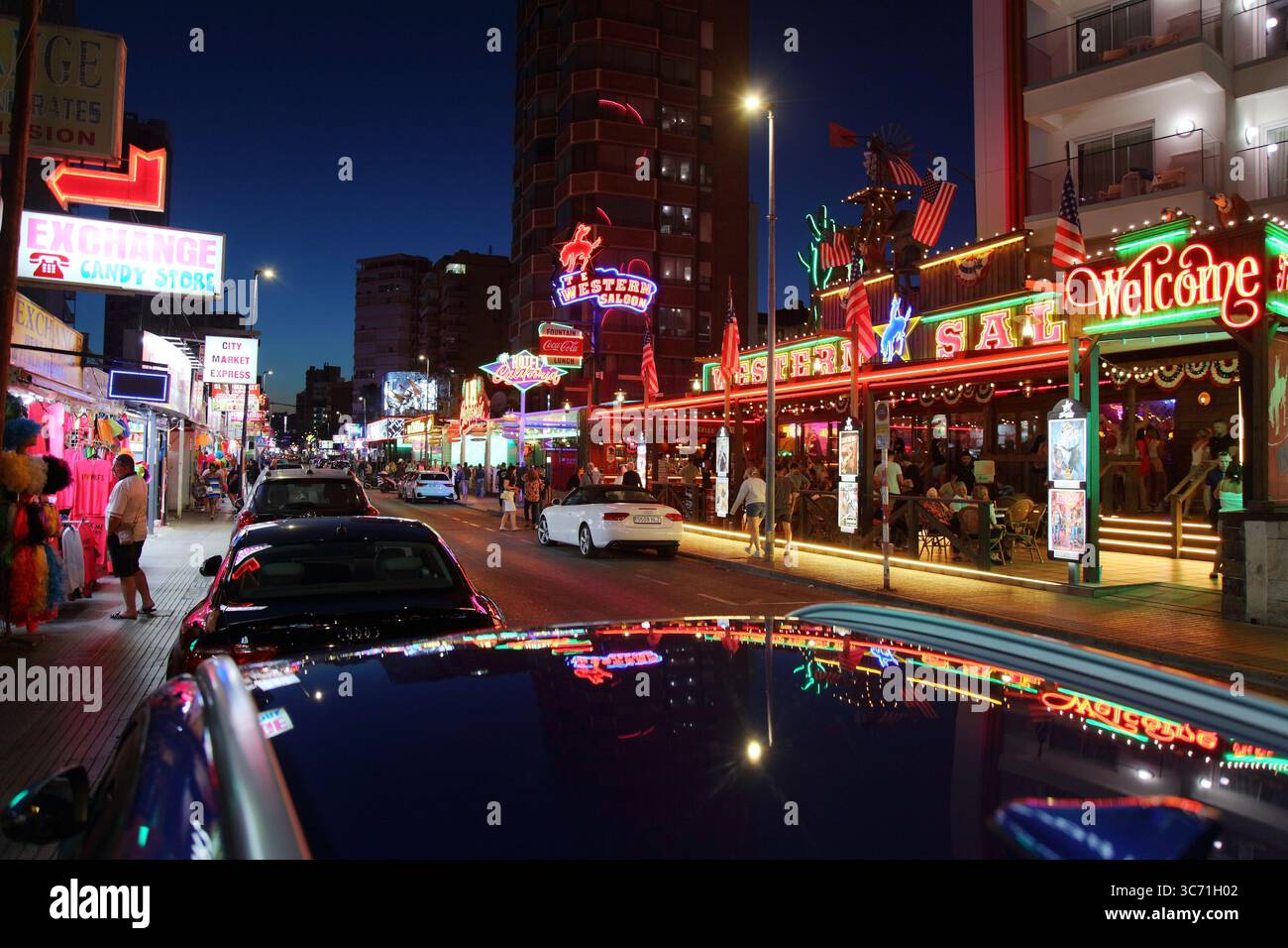 BENIDORM, SPAIN - APRIL 9, 2025: People visit Calle de Gerona street famous for its night life, with pubs, bars and restaurants illuminated with neons Stock Photo