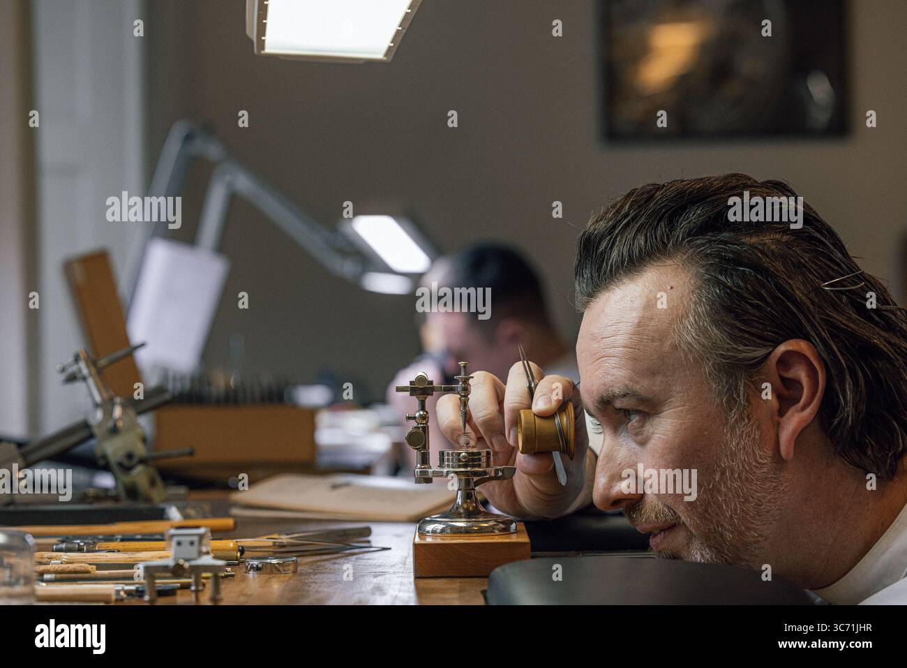 Hervé Schlüchter carefully regulating and cutting a hairspring in his watchmaking atelier, demonstrating the craftsmanship of Swiss horology. Stock Photo