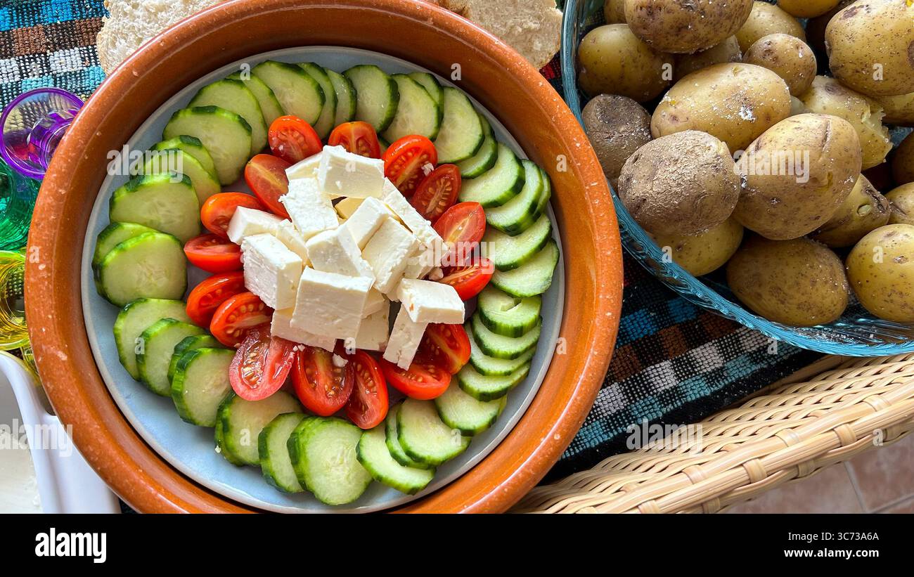 Salad with tomatoes, cucumbers and cheese next to a tray of potatoes Stock Photo