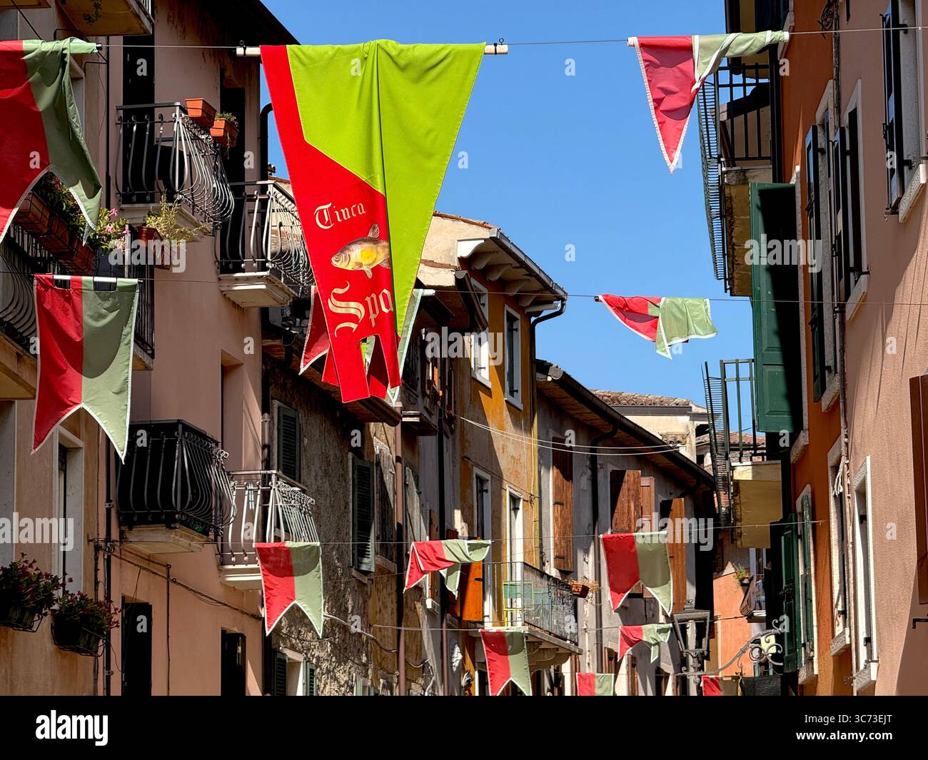 Red and green flags strung over street between houses in Garda, Lake Garda Italy - Smartphone Captured Stock Image