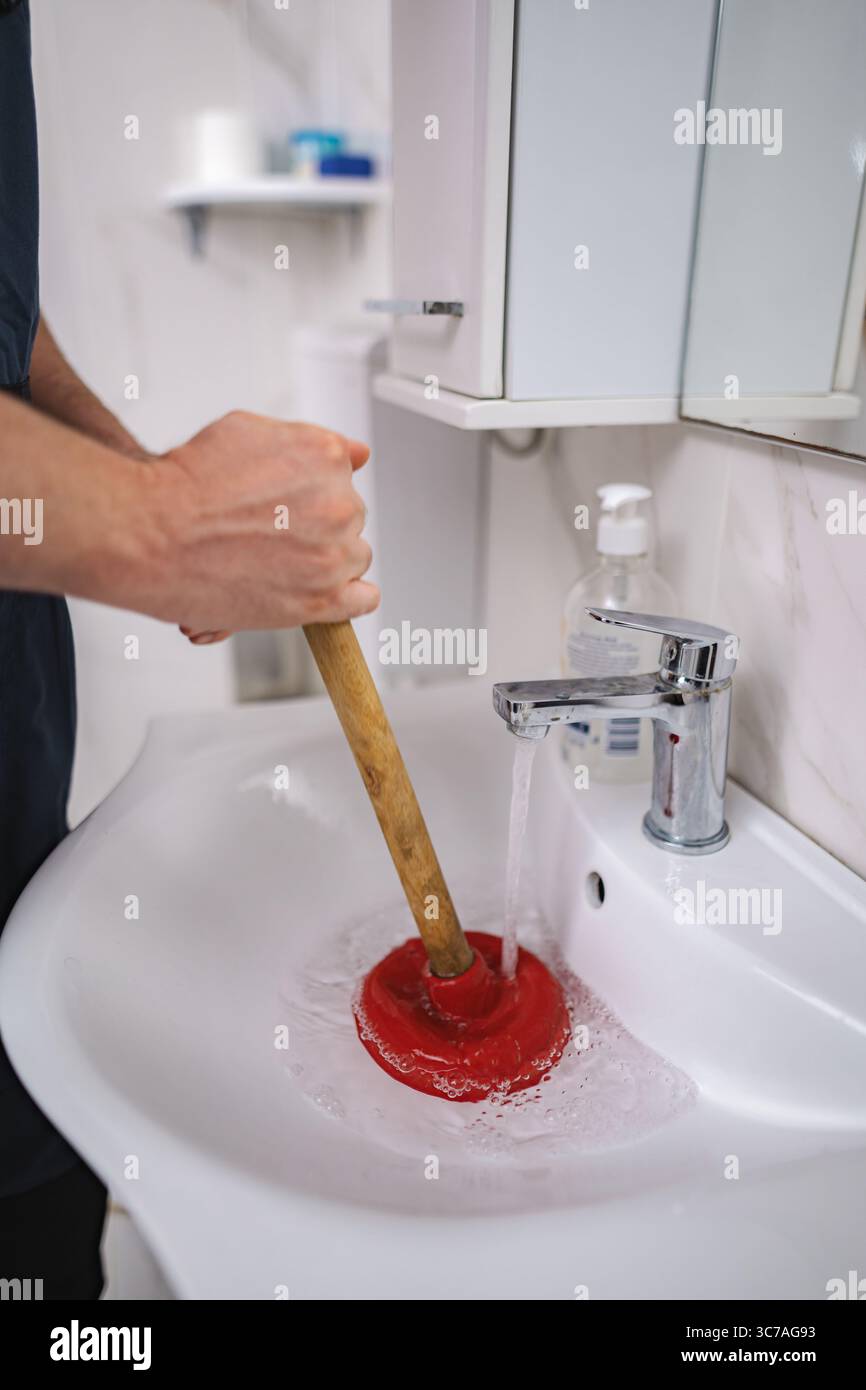 Plumber using plunger in bathroom sink Stock Photo
