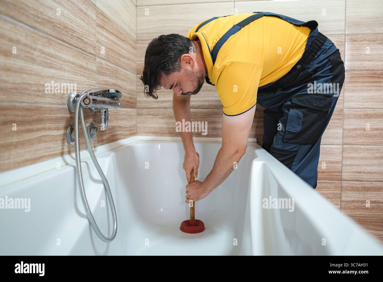 Plumber working to unclog bathtub drain using plunger Stock Photo