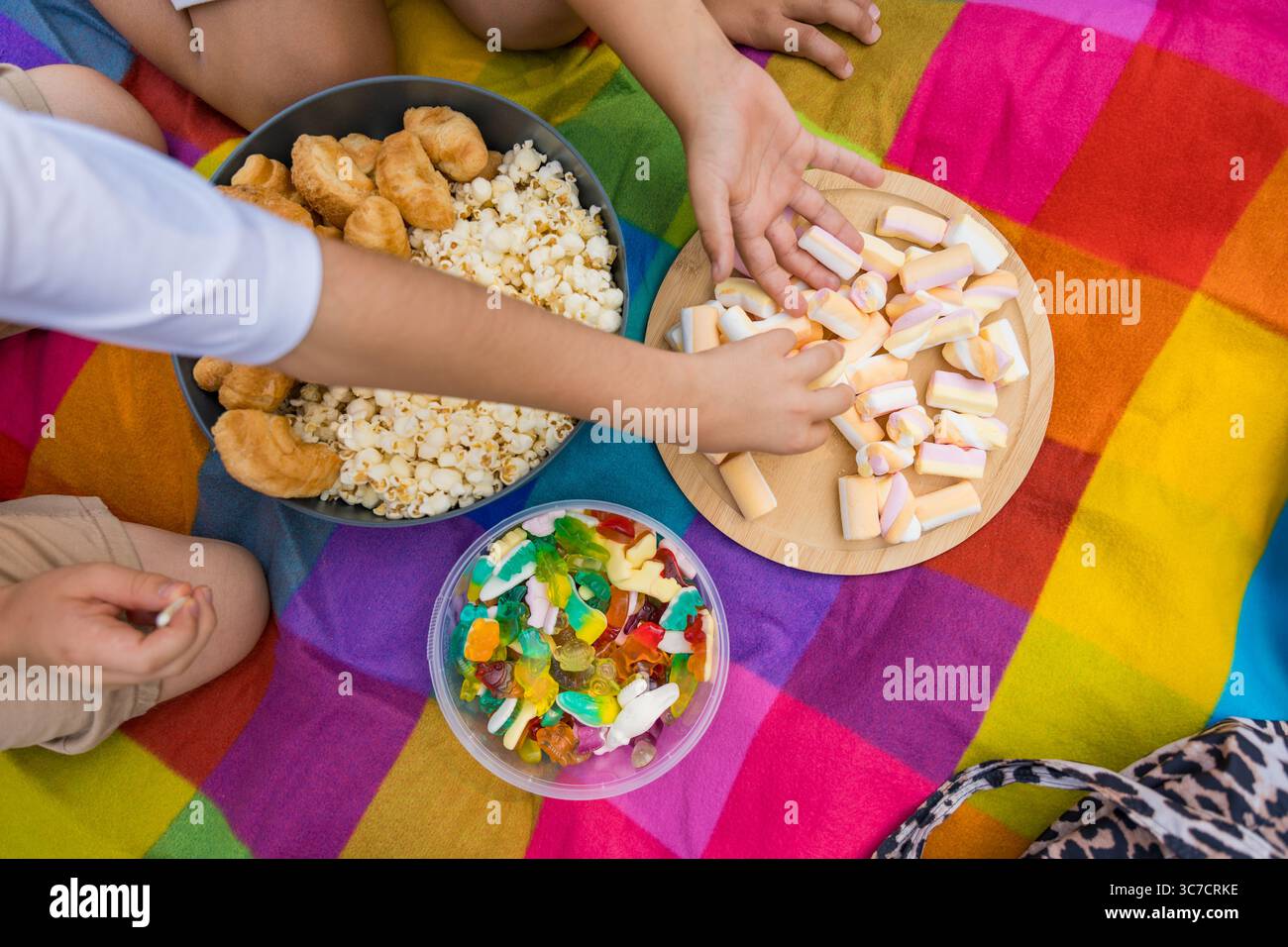 Childrens hands reaching for sweets during colorful picnic on rainbow blanket Stock Photo